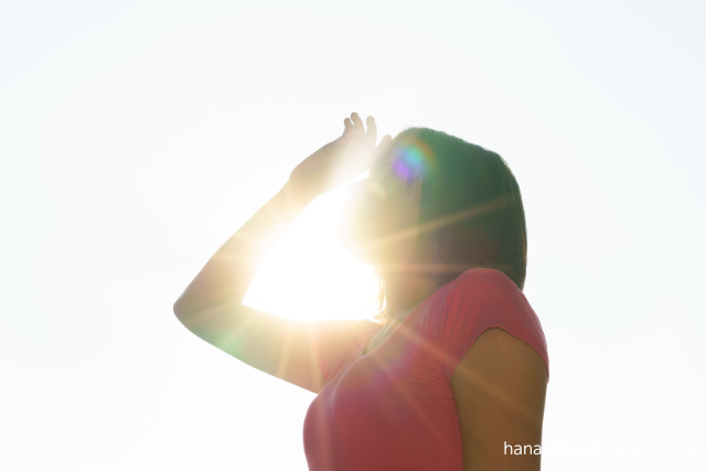まぶしい太陽の光を見上げる女性。夏の日差しを浴びながら、心の中の想いを感じている様子